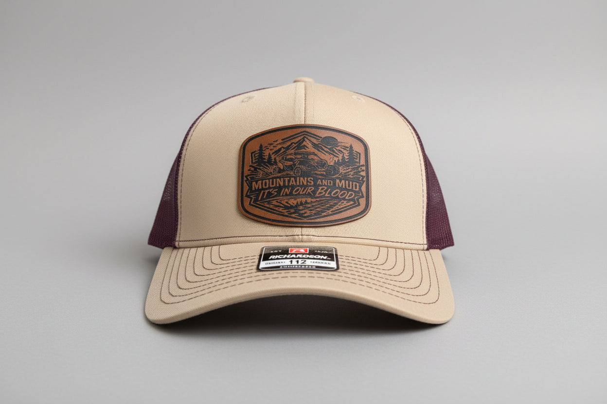 Khaki and maroon trucker hat featuring a leather ‘Mountains and Mud, It’s In Our Blood’ patch on a gray background, Hollarwood Outfitters
