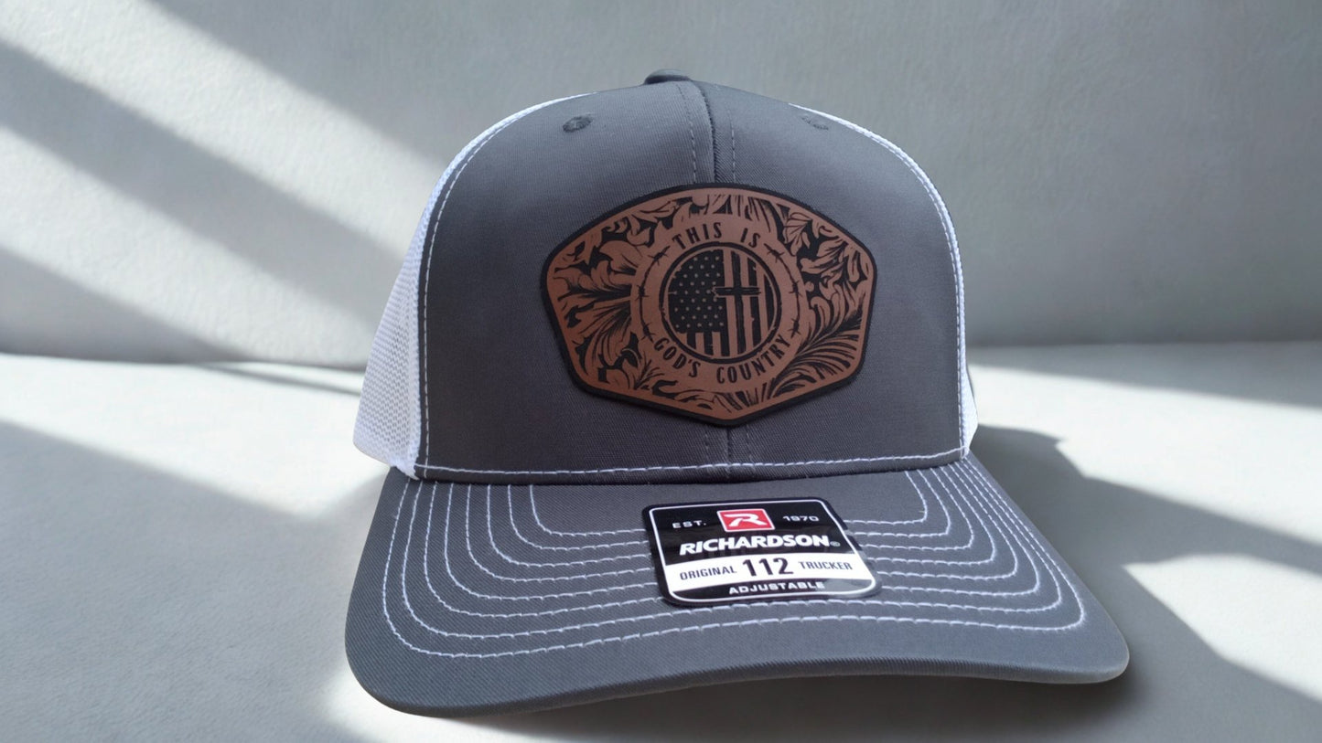 Gray trucker hat featuring a leather ‘God’s Country’ patch on a light background, Hollarwood Outfitters