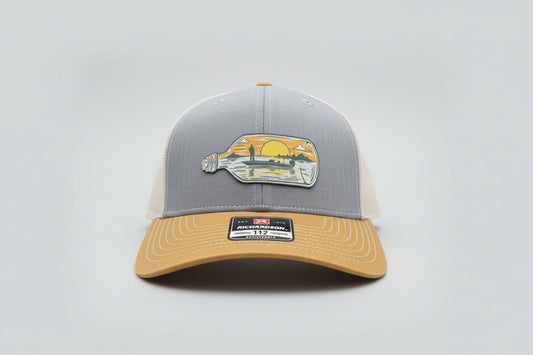 Heather/Birch/Amber Gold trucker hat featuring a castaway fishing bottle patch on a light gray background, Hollarwood Outfitters