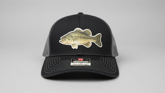 Black and charcoal trucker hat featuring a leather largemouth bass fish‑design patch on a gray background, Hollarwood Outfitters.