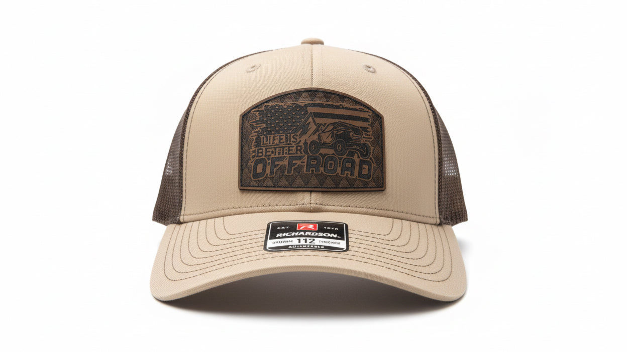 Khaki and chocolate‑brown trucker hat with a leather ‘Life Is Better Off Road’ patch on a white background, Hollarwood Outfitters.